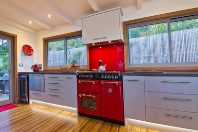 Photo of a mid-sized l-shaped eat-in kitchen in Hamilton with a single-bowl sink, shaker cabinets, beige cabinets, quartz benchtops, red splashback, glass sheet splashback, coloured appliances, bamboo floors and no island.