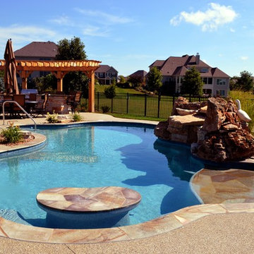 Free form pool with stone table, sun shelf, water feature, and outdoor kitchen,