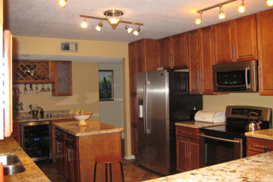 マイアミにある中くらいなトラディショナルスタイルのおしゃれなキッチン (ダブルシンク、レイズドパネル扉のキャビネット、中間色木目調キャビネット、御影石カウンター、シルバーの調理設備) の写真