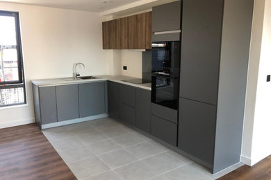 Small modern l-shaped open plan kitchen in Manchester with a single-bowl sink, flat-panel cabinets, grey cabinets, quartz worktops, black appliances, ceramic flooring, grey floors and white worktops.