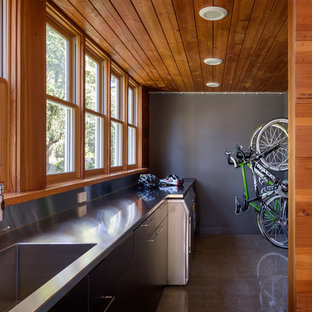 ポートランドの中サイズのモダンスタイルのおしゃれな家事室 (一体型シンク、フラットパネル扉のキャビネット、黒いキャビネット、ステンレスカウンター、グレーの壁、コンクリートの床、左右配置の洗濯機・乾燥機、グレーの床) の写真