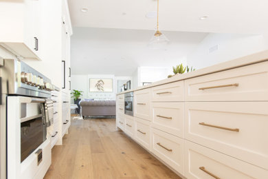 Inspiration for a large eclectic l-shaped light wood floor open concept kitchen remodel in Phoenix with a farmhouse sink, shaker cabinets, white cabinets, quartz countertops, white backsplash, ceramic backsplash, paneled appliances, an island and white countertops