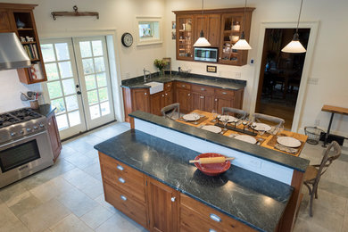 Photo of a country u-shaped kitchen in New York with a farmhouse sink, raised-panel cabinets, medium wood cabinets, soapstone benchtops, subway tile splashback, stainless steel appliances, porcelain floors, with island, grey floor and grey benchtop.
