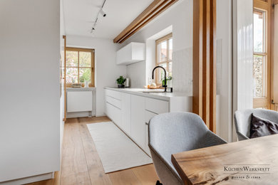 Offene, Zweizeilige, Mittelgroße Moderne Küche ohne Insel mit Unterbauwaschbecken, flächenbündigen Schrankfronten, weißen Schränken, braunem Holzboden und braunem Boden in München