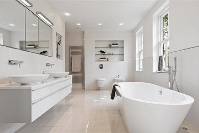 Photo of a large contemporary master bathroom in Denver with flat-panel cabinets, white cabinets, a freestanding tub, a wall-mount toilet, white tile, white walls, porcelain floors, a vessel sink, engineered quartz benchtops and white floor.