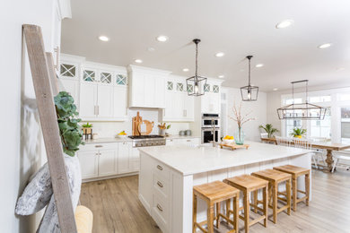 Eat-in kitchen - coastal l-shaped medium tone wood floor and brown floor eat-in kitchen idea in San Luis Obispo with a farmhouse sink, shaker cabinets, white cabinets, white backsplash, stainless steel appliances, an island and white countertops