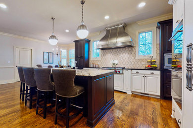 Open concept kitchen - large traditional u-shaped medium tone wood floor and brown floor open concept kitchen idea in Chicago with a farmhouse sink, raised-panel cabinets, white cabinets, granite countertops, beige backsplash, stone tile backsplash, stainless steel appliances, an island and white countertops