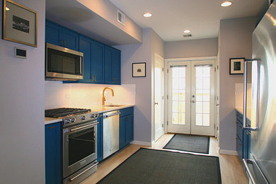 Inspiration for a mid-sized transitional galley light wood floor and tray ceiling enclosed kitchen remodel in New York with an undermount sink, shaker cabinets, blue cabinets, quartz countertops, white backsplash, ceramic backsplash, stainless steel appliances, no island and white countertops