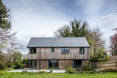 Inspiration for a medium sized and brown contemporary two floor side house exterior in Hampshire with wood cladding, a pitched roof, a mixed material roof, a grey roof and board and batten cladding.