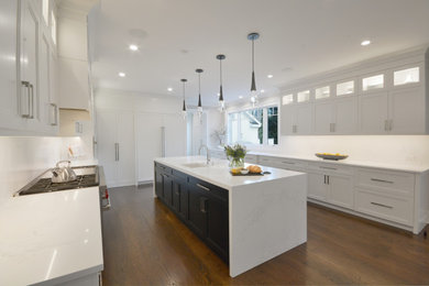Modern galley eat-in kitchen in New York with a farmhouse sink, white cabinets, white splashback, stainless steel appliances, dark hardwood floors, with island, brown floor and white benchtop.