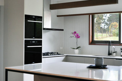 Mid-sized contemporary kitchen in Melbourne with a drop-in sink, grey cabinets, black appliances and light hardwood floors.