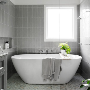 Photo of a transitional bathroom in Melbourne with recessed-panel cabinets, grey cabinets, a freestanding tub, a curbless shower, gray tile, grey walls, multi-coloured floor, an open shower and white benchtops.