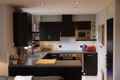 Medium sized contemporary u-shaped open plan kitchen in London with a double-bowl sink, flat-panel cabinets, black cabinets, laminate countertops, white splashback, ceramic splashback, stainless steel appliances, ceramic flooring and a breakfast bar.