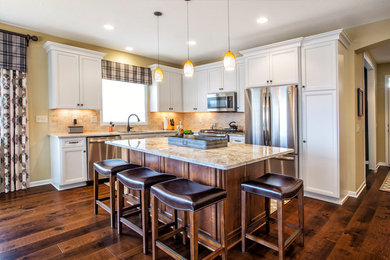 This is an example of a mid-sized traditional l-shaped eat-in kitchen in Minneapolis with an undermount sink, flat-panel cabinets, white cabinets, granite benchtops, beige splashback, travertine splashback, stainless steel appliances, medium hardwood floors, with island and brown floor.