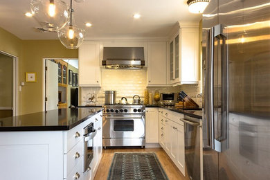 Example of a mid-sized transitional l-shaped light wood floor kitchen design in Orange County with an undermount sink, shaker cabinets, white cabinets, solid surface countertops, white backsplash, ceramic backsplash, stainless steel appliances and an island