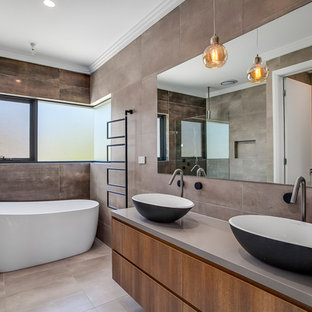 This is an example of a contemporary master bathroom in Sydney with flat-panel cabinets, brown cabinets, a freestanding tub, brown tile, gray tile, grey walls, a vessel sink, grey floor and grey benchtops.