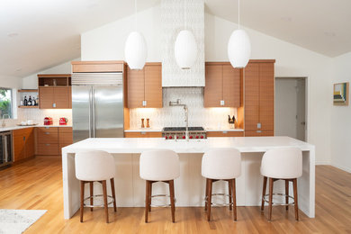 Eat-in kitchen - large mid-century modern medium tone wood floor, brown floor and vaulted ceiling eat-in kitchen idea in Seattle with a farmhouse sink, flat-panel cabinets, medium tone wood cabinets, quartz countertops, white backsplash, ceramic backsplash, stainless steel appliances, an island and white countertops