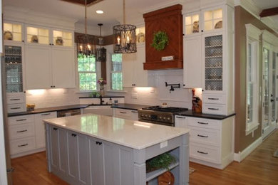 Design ideas for a medium sized classic u-shaped open plan kitchen in Raleigh with a belfast sink, recessed-panel cabinets, white cabinets, engineered stone countertops, white splashback, stainless steel appliances, light hardwood flooring, an island, beige floors and white worktops.