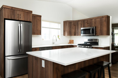 This is an example of a small modern l-shaped kitchen/diner in Calgary with a submerged sink, flat-panel cabinets, dark wood cabinets, quartz worktops, white splashback, ceramic splashback, stainless steel appliances, light hardwood flooring, an island, brown floors, white worktops and a vaulted ceiling.