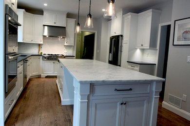 Inspiration for a large transitional u-shaped eat-in kitchen in New York with a farmhouse sink, flat-panel cabinets, white cabinets, marble benchtops, white splashback, ceramic splashback, stainless steel appliances, medium hardwood floors and with island.