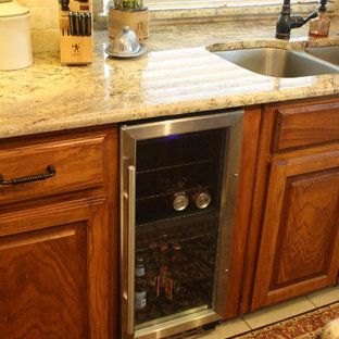 Cette photo montre une grande arrière-cuisine parallèle montagne avec un évier posé, un placard à porte shaker, des portes de placard en bois brun, un plan de travail en granite, une crédence beige, une crédence en carrelage de pierre, un électroménager en acier inoxydable, un sol en carrelage de porcelaine et un îlot central.