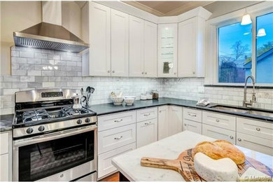 Mid-sized transitional l-shaped medium tone wood floor enclosed kitchen photo in Denver with an undermount sink, shaker cabinets, white cabinets, soapstone countertops, white backsplash, stone tile backsplash, stainless steel appliances and an island