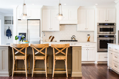 This is an example of a mid-sized traditional l-shaped eat-in kitchen in Nashville with shaker cabinets, white cabinets, solid surface benchtops, white splashback, subway tile splashback, stainless steel appliances, dark hardwood floors, with island and brown floor.