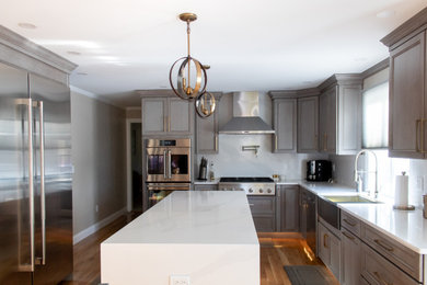Example of a large trendy u-shaped light wood floor and brown floor eat-in kitchen design in Boston with a farmhouse sink, flat-panel cabinets, gray cabinets, quartzite countertops, white backsplash, quartz backsplash, stainless steel appliances, an island and white countertops