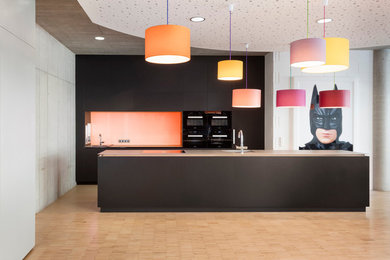 Offene, Zweizeilige, Mittelgroße Moderne Küche mit Einbauwaschbecken, flächenbündigen Schrankfronten, schwarzen Schränken, Edelstahl-Arbeitsplatte, bunter Rückwand, Glasrückwand, Küchengeräten aus Edelstahl, Keramikboden und Kücheninsel in Stuttgart