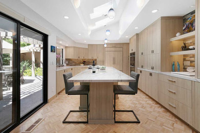 Example of a large trendy l-shaped plywood floor, beige floor and vaulted ceiling eat-in kitchen design in San Francisco with an undermount sink, flat-panel cabinets, light wood cabinets, multicolored backsplash, stone tile backsplash, paneled appliances, an island and white countertops
