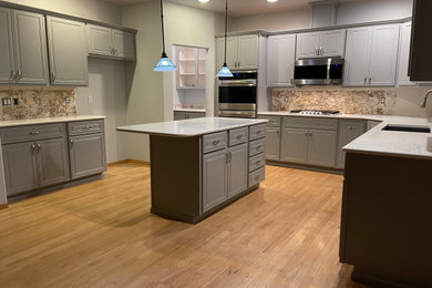 Example of a large transitional u-shaped light wood floor and brown floor eat-in kitchen design in Tampa with an undermount sink, shaker cabinets, gray cabinets, quartz countertops, stainless steel appliances, an island and white countertops