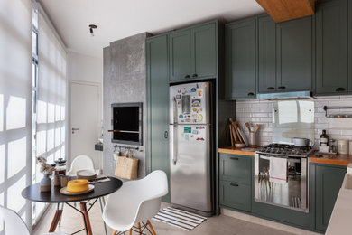 Urban porcelain tile, gray floor and exposed beam kitchen photo in Frankfurt with a farmhouse sink, green cabinets, wood countertops, white backsplash, ceramic backsplash, stainless steel appliances and brown countertops