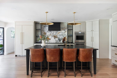 Inspiration for a large transitional l-shaped light wood floor and brown floor open concept kitchen remodel in Austin with an undermount sink, recessed-panel cabinets, beige cabinets, granite countertops, multicolored backsplash, marble backsplash, paneled appliances, an island and black countertops