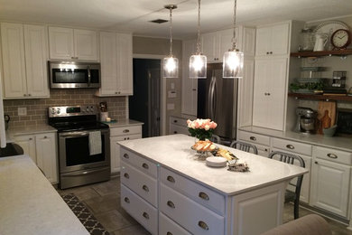 Example of a mid-sized classic l-shaped ceramic tile and beige floor enclosed kitchen design in Jacksonville with a farmhouse sink, raised-panel cabinets, white cabinets, quartzite countertops, beige backsplash, subway tile backsplash, stainless steel appliances and an island
