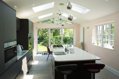 Modern cream and black kitchen in Buckinghamshire with a built-in sink, flat-panel cabinets, black cabinets, marble worktops, stainless steel appliances, laminate floors, an island, grey floors, white worktops, a vaulted ceiling and feature lighting.