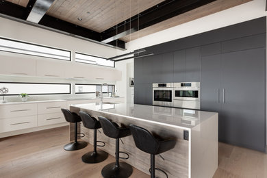 Eat-in kitchen - large contemporary l-shaped medium tone wood floor and brown floor eat-in kitchen idea in Vancouver with flat-panel cabinets, black cabinets, quartz countertops, paneled appliances, an island and white countertops