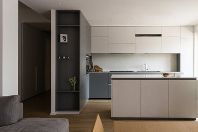 Esempio di una cucina minimalista di medie dimensioni con lavello integrato, ante lisce, ante grigie, top in acciaio inossidabile, paraspruzzi bianco, elettrodomestici in acciaio inossidabile e parquet chiaro