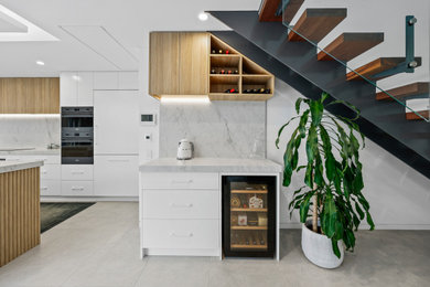 Inspiration for a large mediterranean l-shaped open plan kitchen in Sydney with a farmhouse sink, quartz benchtops, white splashback, engineered quartz splashback, black appliances, porcelain floors, with island, grey floor, white benchtop and recessed.
