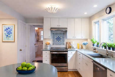 Inspiration for a mid-sized transitional l-shaped medium tone wood floor and brown floor enclosed kitchen remodel in New York with a drop-in sink, flat-panel cabinets, white cabinets, soapstone countertops, white backsplash, ceramic backsplash, stainless steel appliances, an island and blue countertops
