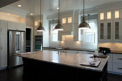 Transitional l-shaped eat-in kitchen photo in Indianapolis with a farmhouse sink, shaker cabinets, white cabinets, granite countertops, white backsplash, subway tile backsplash, stainless steel appliances and an island