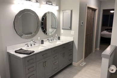 Photo of a mid-sized contemporary master bathroom in Calgary with shaker cabinets, grey cabinets, marble benchtops, a corner shower, white tile, subway tile, grey walls, porcelain floors, an undermount sink, grey floor and a hinged shower door.