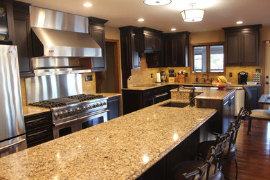Eat-in kitchen - large traditional l-shaped medium tone wood floor and brown floor eat-in kitchen idea in Chicago with stainless steel appliances, an undermount sink, dark wood cabinets, quartzite countertops, beige backsplash, stone tile backsplash, an island and raised-panel cabinets