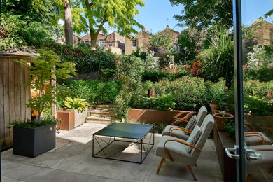 Medium sized contemporary back patio in London with a potted garden and natural stone paving.