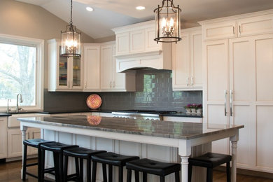 Inspiration for a large transitional l-shaped medium tone wood floor eat-in kitchen remodel in Cincinnati with a farmhouse sink, recessed-panel cabinets, white cabinets, granite countertops, gray backsplash, ceramic backsplash, an island and paneled appliances