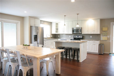 Large farmhouse l-shaped dark wood floor eat-in kitchen photo in Boise with raised-panel cabinets, white cabinets, granite countertops, gray backsplash, porcelain backsplash, stainless steel appliances and an island