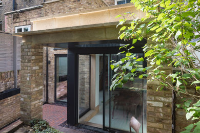 Design ideas for a small contemporary back patio in London with brick paving and a roof extension.