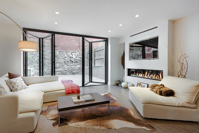 Example of a trendy medium tone wood floor family room design in New York with white walls, a ribbon fireplace, a media wall and a concrete fireplace