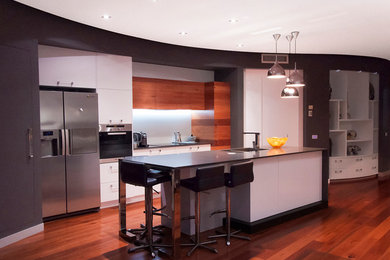 Inspiration for a mid-sized contemporary galley eat-in kitchen in Brisbane with an undermount sink, flat-panel cabinets, medium wood cabinets, quartz benchtops, white splashback, glass sheet splashback, stainless steel appliances, medium hardwood floors and with island.