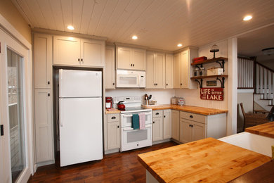 Inspiration for a mid-sized cottage u-shaped dark wood floor and brown floor open concept kitchen remodel in Indianapolis with a farmhouse sink, shaker cabinets, white cabinets, wood countertops, white backsplash, wood backsplash, white appliances and a peninsula
