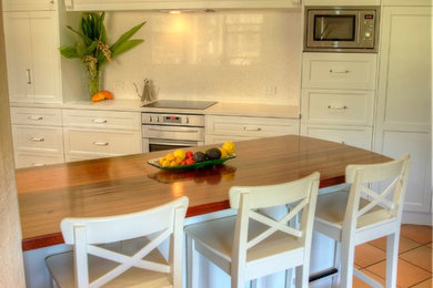Design ideas for a mid-sized country galley eat-in kitchen in Other with a farmhouse sink, shaker cabinets, white cabinets, quartz benchtops, white splashback, stone tile splashback, stainless steel appliances, terra-cotta floors and a peninsula.